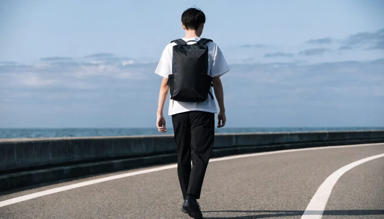 海沿いの道を小さな黒いデイパックで歩く男性の後ろ姿のイメージ